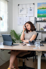 A woman is sitting at a desk with a laptop and a cell phone. She is talking on the phone and she is in a serious mood