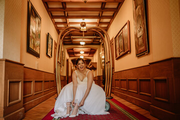 Valmiera, Latvia - August 19, 2023 - A joyful bride sits on the floor in a hotel hallway, laughing...