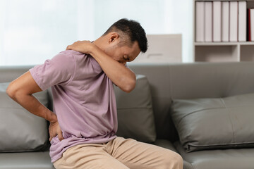 Asian man with back pain Massaging sore muscles while sitting on the sofa, elderly people and health problems concept.