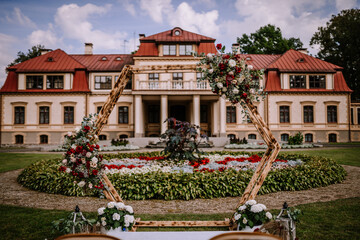 Valmiera, Latvia - August 19, 2023 - A floral archway stands in front of a stately mansion with gardens, an elegant setting for a wedding or event.