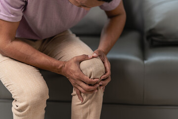 Knee pain sick body health care concept A young man has knee pain, sitting on the sofa at home,...
