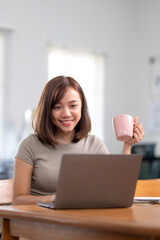 A woman is sitting at a table with a laptop and a pink cup