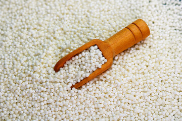 White sago pearls in a wooden scoop on a sago background.