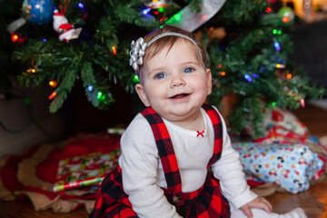 Baby girl smiling by Christmas tree in festive outfit