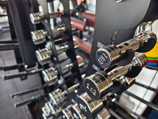 A rack of stainless steel or chrome coated dumbbells of various weights at a gym or fitness club.