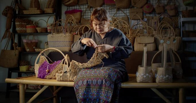Slow motion scene while an Asian female artisan who is a local villager knitting folk basket made from leftover paper band to sell as extra income in the basketry shop shop.