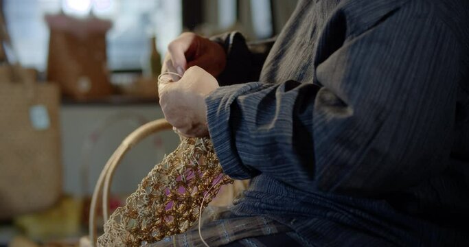 Slow motion scene while an Asian female artisan who is a local villager knitting folk basket made from leftover paper band to sell as extra income in the basketry shop shop.