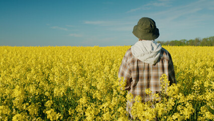 Young woman farmer standing in yellow rapeseed field, rear view