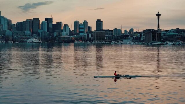 A single rower in a boat paddles their way across Lake Union in Seattle with the skyline and space needle in the background