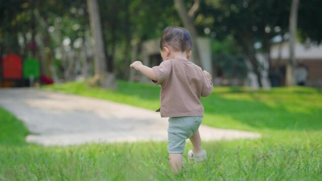 Shot from behind of asian boy walking on the green grass field, Healthy active lifestyle of child in the park childhood, family outdoor activity for kid learning skill, innocence child first step