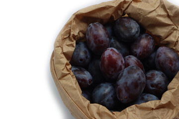 Close-up of purple plums in a brown paper bag isolated on white background. Prunus domestica  fruits