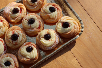 Italian traditional fried Zeppole on a golden cardboard tray for St. Joseph (Father’s day). Homemade sweet pastry with custard cream and black cherries in syrup