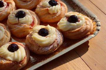 Italian traditional fried Zeppole on a golden cardboard tray for St. Joseph (Father’s day). Homemade sweet pastry with custard cream and black cherries in syrup