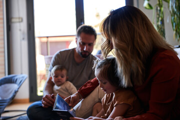 Mother and daughter reading a book while father and baby are looking them