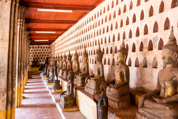 row of historic sitting buddhas in a hallway of a temple in Vientiane, Laos