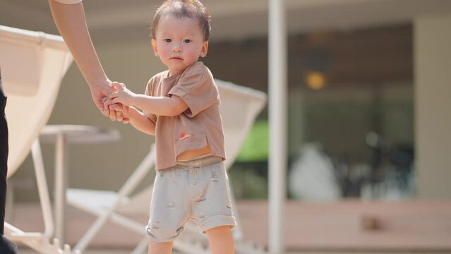 Asian adorable baby boy try to escape from his mother's hand while walking outside. Travel with kid. Cute curious playful infant holding hand going out with babysitter. Family leisure weekend activity