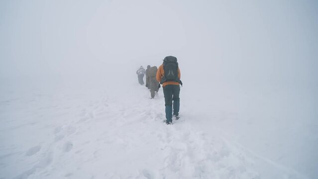 Climbing Everest. Extreme climbing, A group of tourists and men with backpacks climb Everest with ski poles, make their way through strong winds and blizzards. Heavy snowfall, low visibility