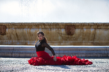 Beautiful woman dancing flamenco in a square in Seville, Spain. She is wearing a typical red and...