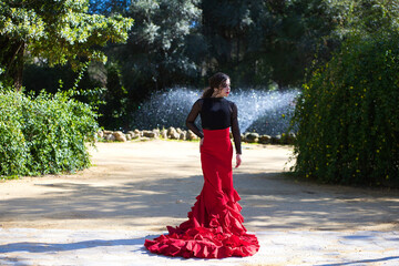 Beautiful woman dancing flamenco in Seville, Spain. She wears a red and black gypsy dress and dances flamenco with a lot of art. In the background a fountain. Flamenco, cultural heritage of humanity.