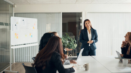 CEO laughing while giving a whiteboard presentation to businesswomen in an office