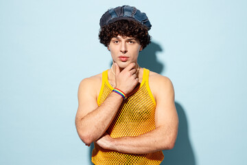 Young confident attractive cool gay Latin man wear mesh tank top hat clothes prop up chin look camera isolated on plain pastel light blue cyan background studio Pride day June month love LGBT concept