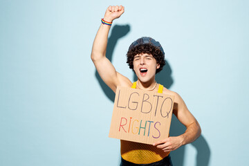 Young happy gay Latin man wear mesh tank top hat clothes hold card with LGBTQ rights title text isolated on plain pastel blue cyan background studio portrait. Pride day June month love LGBT concept.