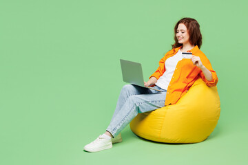 Full body young IT woman wear orange shirt t-shirt casual clothes sit in bag chair using laptop pc...