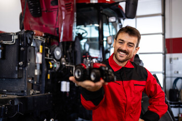 Experienced serviceman holding tractor model inside workshop.