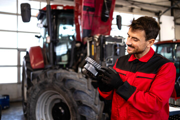 Professional serviceman servicing tractor gears transmission inside workshop.