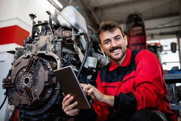 Portrait of smiling tractor mechanic holding tablet computer and standing by the engine.