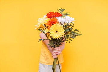 A child holds a large multi-colored bouquet in front of him against a yellow background