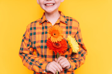 Boy in a shirt holding flowers in his hands against a yellow background.