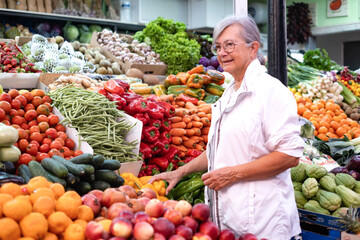 Senior woman buying fresh fruit and vegetables at the market, choosing from a large selection. Healthy eating, the concept of spending and consumerism