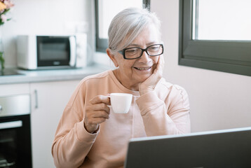 Smiling old caucasian businesswoman working online watching funny webinar podcast on laptop and...