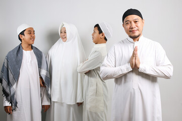 Asian muslim man in skullcap showing greeting hands gesture while his family on the background