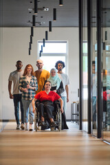 Fototapeta premium A diverse group of young business people walking a corridor in the glass-enclosed office of a modern startup, including a person in a wheelchair and a woman wearing a hijab