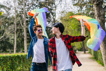 A vibrant day as a Chinese and Latino gay couple enjoy the outdoors, waving colorful LGBT tail fans