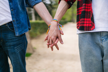 Hands with colorful LGBT wristbands held by a loving male couple, standing in a serene park.