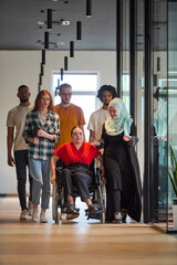 Fototapeta premium A diverse group of young business people walking a corridor in the glass-enclosed office of a modern startup, including a person in a wheelchair and a woman wearing a hijab