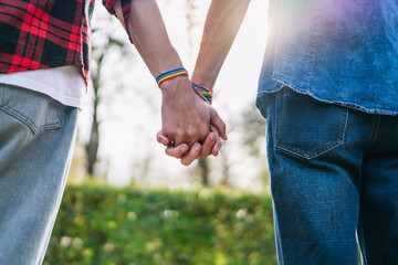 Two men hand in hand, their wrists highlighted by colorful LGBT bracelets, signifying solidarity.