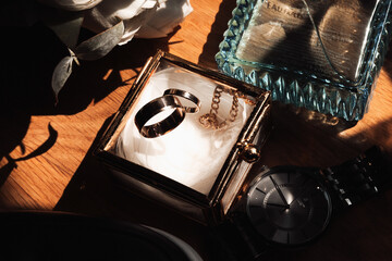 A couple's wedding rings are displayed in a glass box on a table. A watch is also on the table