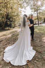 A bride and groom are standing in a park, with the bride wearing a white dress and the groom wearing a black suit