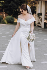 A woman in a white dress is walking down a path with a bouquet of flowers in her hand