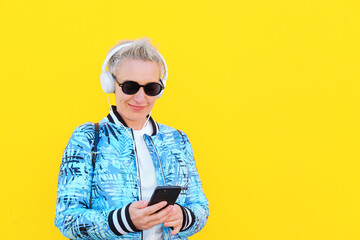 Middle Aged Woman, Short HairStyle, Casual Look With White Headphones On Yellow Background....