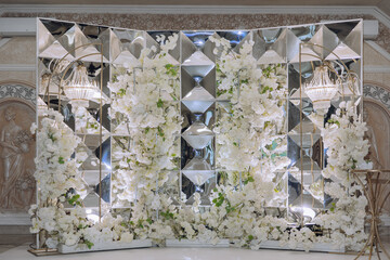 A large wall of white flowers with a gold frame. The flowers are arranged in a way that they look like they are growing out of the wall. Scene is elegant and sophisticated
