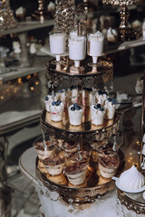 A dessert table with a variety of desserts, including blueberry cheesecake. The table is set up with a three-tiered display, and the desserts are served in small cups