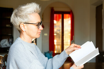 Middle-Aged Mature Businesswoman Holding And Looking At An Empty White Paper Book In The Home...