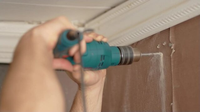 Economical renovation in old apartment. Man drills wall with hammer drill in his home, close up. Male drills wall to hang cornice
