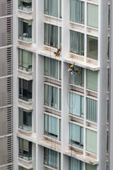 Two men at the exterior of a high-rise building. One working at height cleaning window and the...