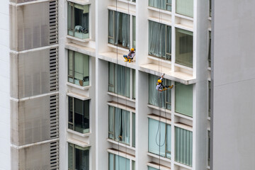 Two men at the exterior of a high-rise building. One working at height cleaning window and the other one sleeping on the job